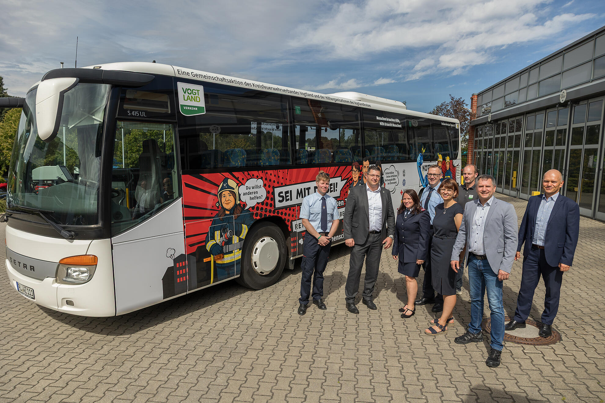 Übergabe der Schulbusse mit Ehrenamtsmotiven. Von links nach rechts: Kreisbrandmeister Gerd Pürzel, Landrat Thomas Hennig, Feuerwehrfrau Sandra Neubert, Geschäftsstellenleiter des Kreisfeuerwehrverbandes Vogtland e.V. Daniel Löwenhagen, POB-Kaufmännische Leiterin Christiane Fischer, POB- Prokurist Stefan Weller, VVV-Geschäftsführer Michael Barth, POB-Geschäftsführer Thomas Schwui