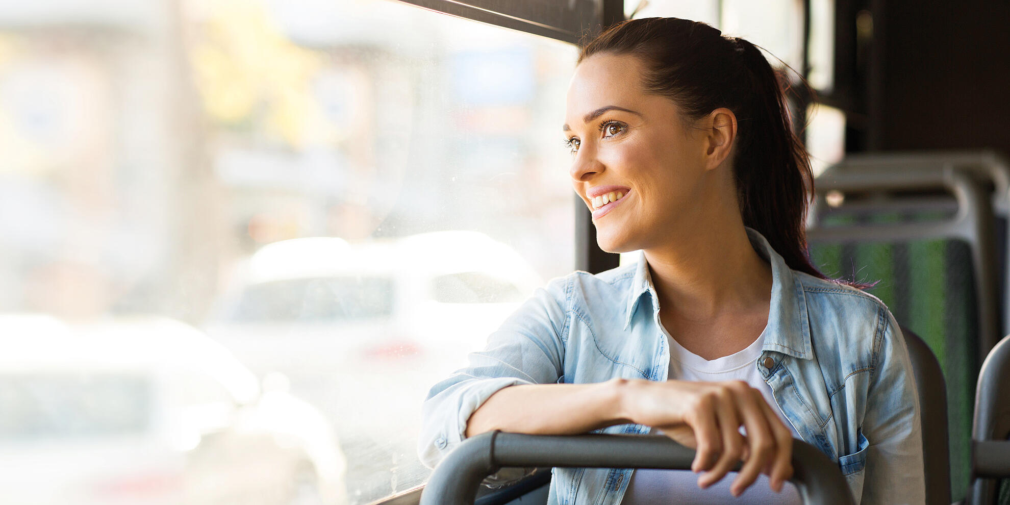 Kampagnenmotiv Pendler: lächelnde Frau sitzt im Bus und schaut aus dem Fenster