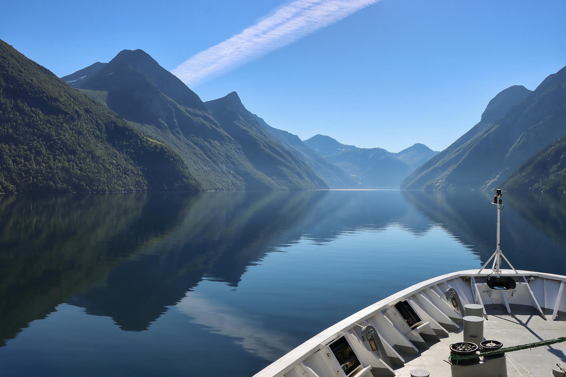 Die Spitze eines Schiffes ragt in den Stor­fjord hinein, umgeben von steilen, dunklen Bergen und ruhigem Wasser.