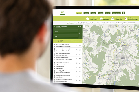 Person blickt auf einen Computerbildschirm mit einer digitalen Karte und Suchfunktion für Fahrplanauskünfte im öffentlichen Nahverkehr.